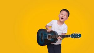 Child playing guitar, promoting music education for blind and visually impaired children through Vision Through Music program.